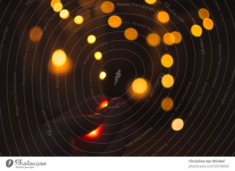 Playfulness with fairy lights and candlelight. Hand holds a string of lights. Defocused points of light in front of dark background. Fairy lights Light shine