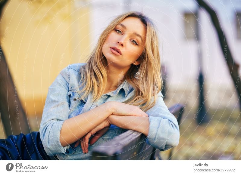 Blonde woman wearing denim shirt and black leather skirt sitting in an urban bench. girl female blonde russian blue eyes portrait fashion outdoors lady