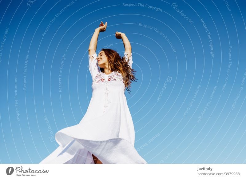 Young woman raising her arms in a beautiful white dress against a blue sky fashion girl wave open hair female copyspace extensions hairstyle fashionable model