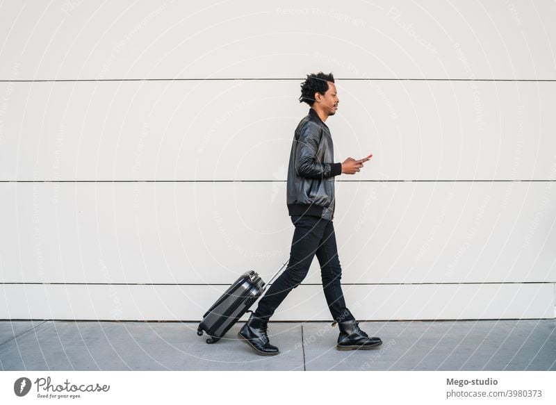 Tourist man using his mobile phone and carrying suitcase outdoors. tourist communication business text black cell sms holiday city journey enjoy telephone afro