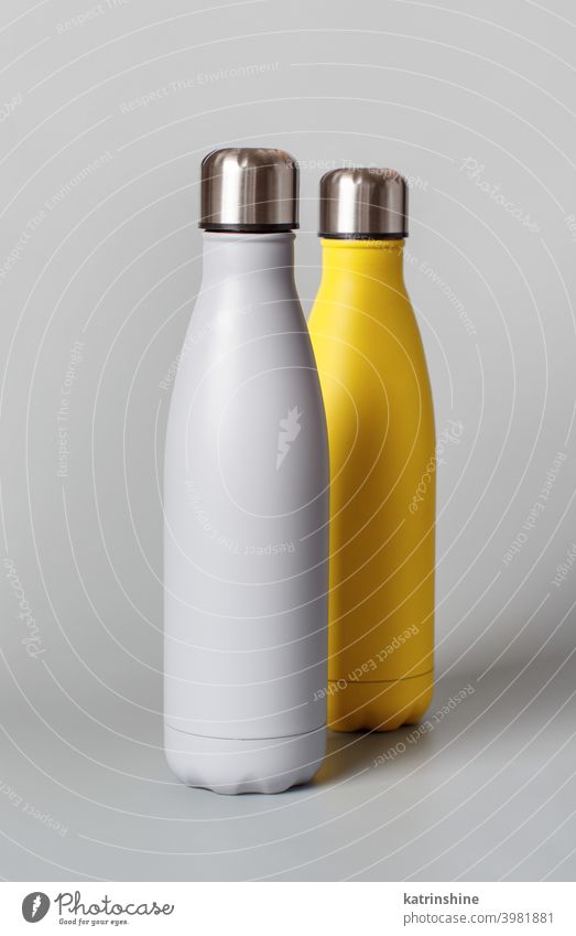 Grey and yellow reusable bottles on grey background monochrome mockup insulated ecologic water steel thermo aluminum blank close up concept copy space