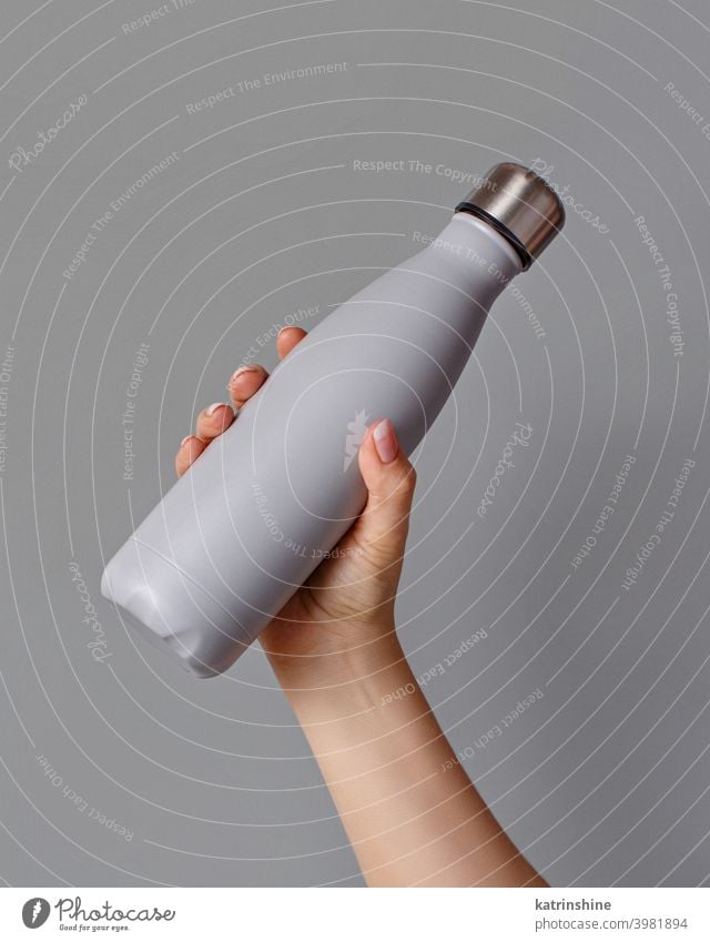 Hand with grey rinsulated bottle on grey background reusable hand monochrome mockup yellow ecologic water steel thermo aluminum blank close up concept