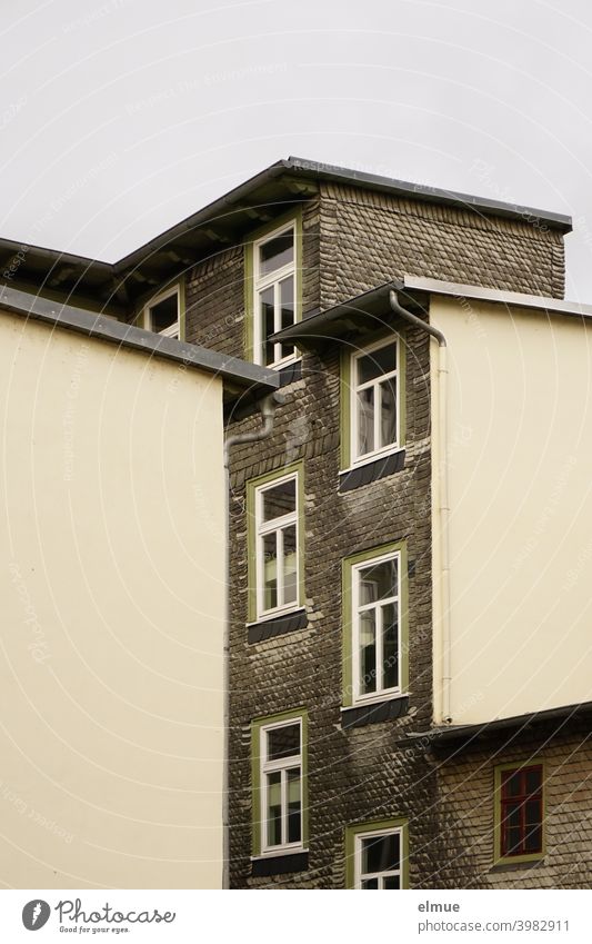 View into a courtyard of a renovated slate house with numerous staggered windows Apartment Building schieferhaus Disguised Renovated dwell Facade Backyard shale