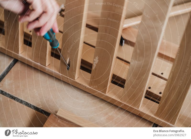 close up of young woman assembling furniture at home working with screwdriver. DIY concept mobile phone do it yourself technology internet help instructions