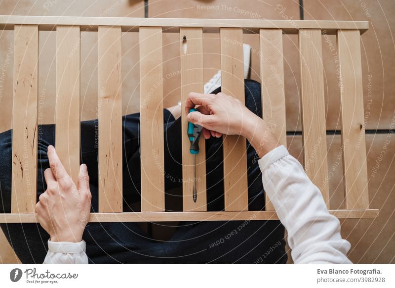 close up of young woman assembling furniture at home working with screwdriver. DIY concept mobile phone do it yourself technology internet help instructions