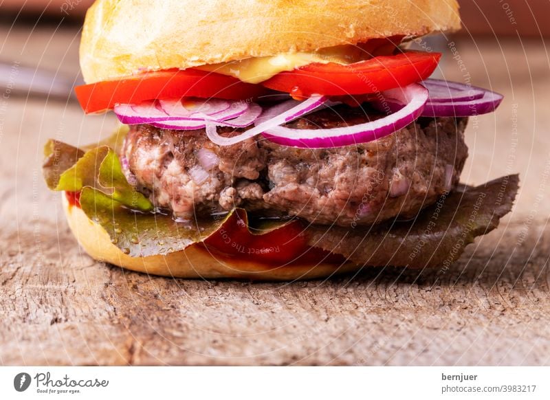 Close up of a hamburger on wood Hamburger Cheeseburger Minced meat Meat homemade ingredient BBQ swift Roll Onion Red OnionRing grilled Lettuce Eating Fat Snack