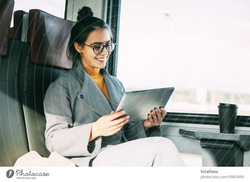 Young girl on the train communicating on the tablet with friends and relatives while traveling on the train woman passenger happy reading ebook inside online