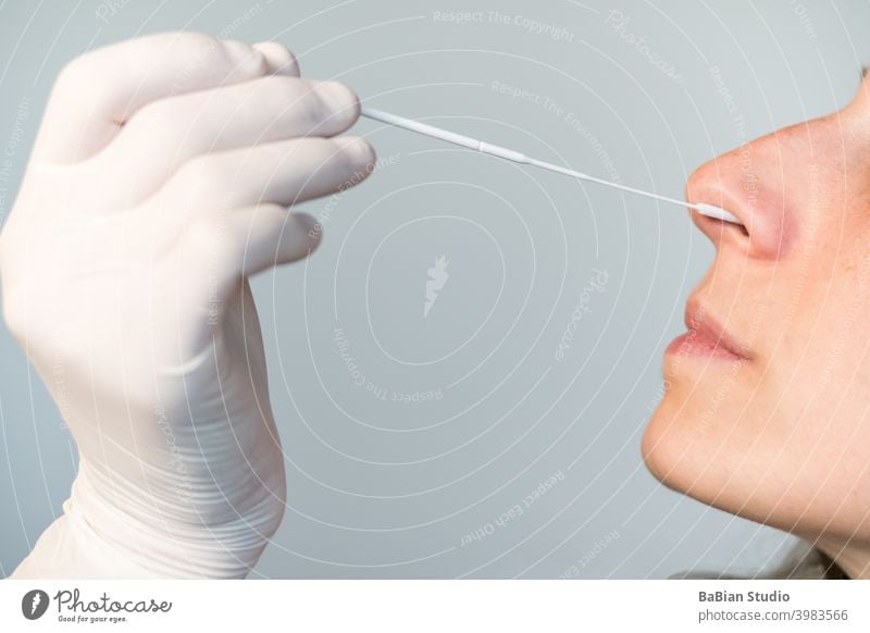 A nurse wearing latex gloves inserts a swab into a woman's nose to collect a possible positive COVID-19 sample during the pandemic. Antigen test procedure.