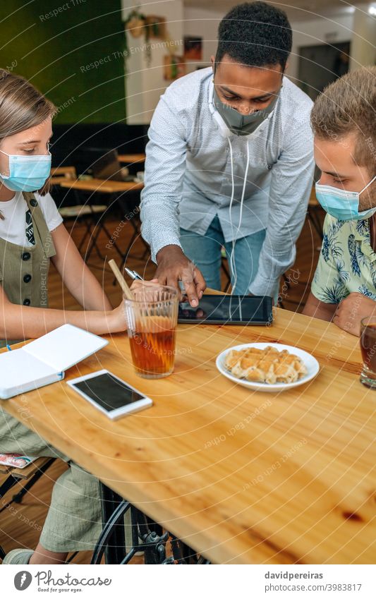 Young people looking at the tablet in a coffee shop friends talking smiling protective mask coronavirus planning trip young cafeteria booking restaurant lunch