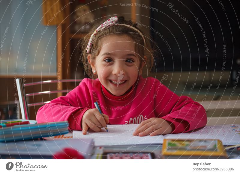 Smiling 6 year old girl does her homework child smiling write writing table case colors pens learning study schoolgirl desk childhood lesson student studying