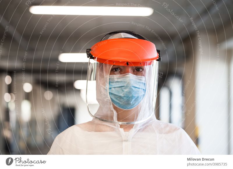 Portrait of female paramedic wearing personal protective equipment, face mask and face shield, standing in a hospital hallway or corridor ambulance background