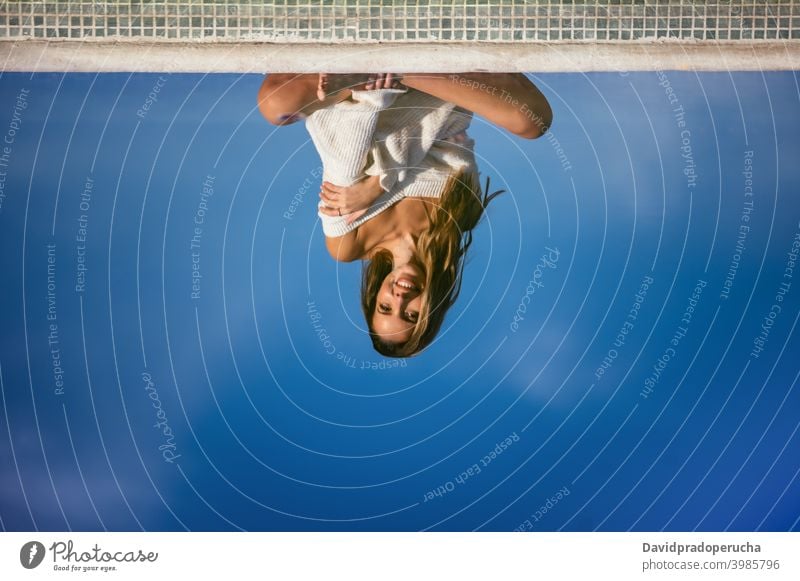 Crop woman resting near pool reflection water smile happy yard daytime calm legs crossed barefoot summer sit relax poolside lifestyle cheerful idyllic