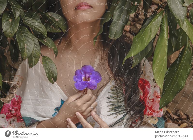 Woman wearing a floral summer dress and holding a flower to her chest, showing concept of mindfulness, meditation, spring season and life new beginnings blossom