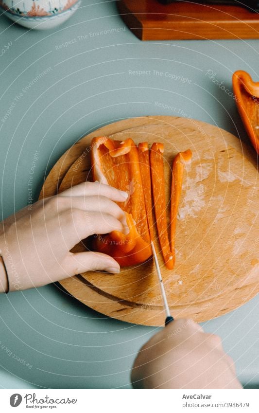 A woman cutting some pepper over a wooden round plate with a knife while cooking with the pan in the kitchen horizontal workplace desktop person indoors