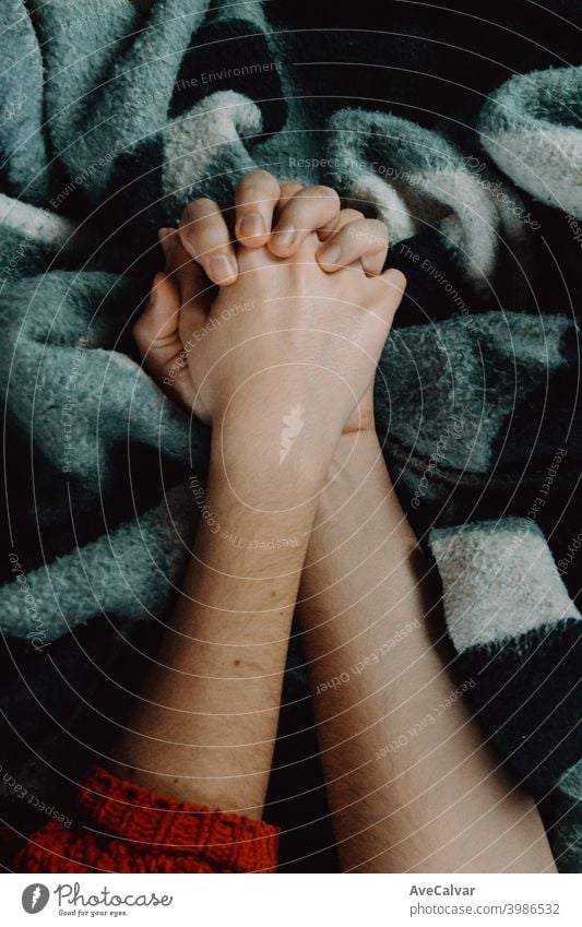 A pair of hands holding each other over a blue and grey blanket closeness mature middle aged relationship together togetherness holding hands love people bed