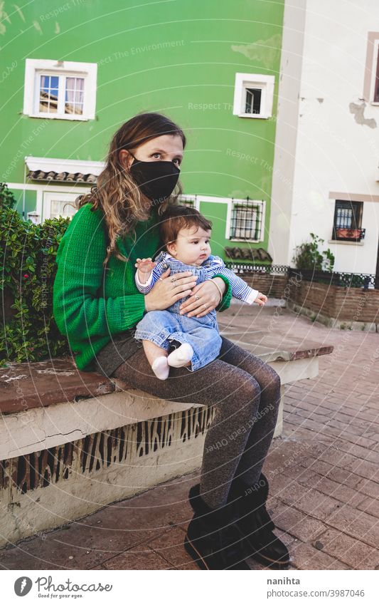 Image in green tones of a young single mom with her baby during covid pandemic coronavirus mother family motherhood mask face mask risk contagious influenza