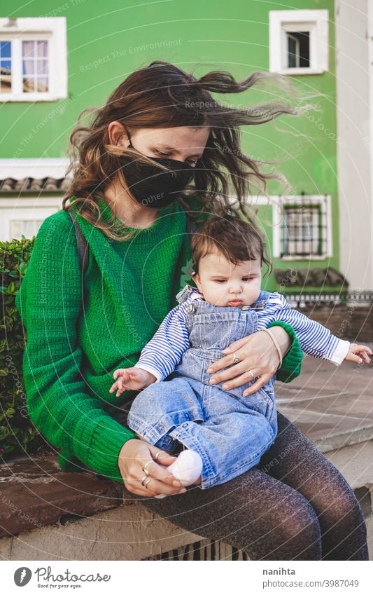 Image in green tones of a young single mom with her baby during covid pandemic coronavirus mother family motherhood mask face mask risk contagious influenza