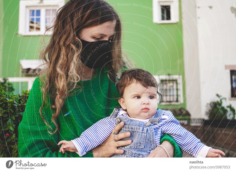 Image in green tones of a young single mom with her baby during covid pandemic coronavirus mother family motherhood mask face mask risk contagious influenza