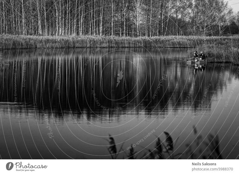 two fishermen in a boat with reflection in a still river water at twilight on autumn landscape. Alone anchor beautiful Latvia berth birch boating canoe chain