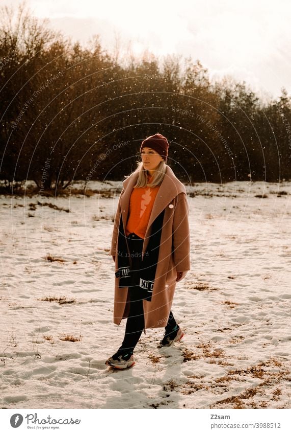 Fashionably dressed young woman walking in light snowfall stroll Winter wonderland Woman Young woman Coat To go for a walk Snow Sun Light Nature Landscape Scarf