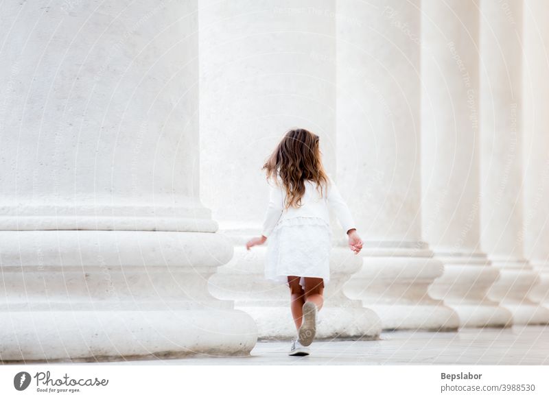 Rear view of a pretty little girl running next to the collonade child females childhood fun game joy children serenity column person playing outdoor street kid