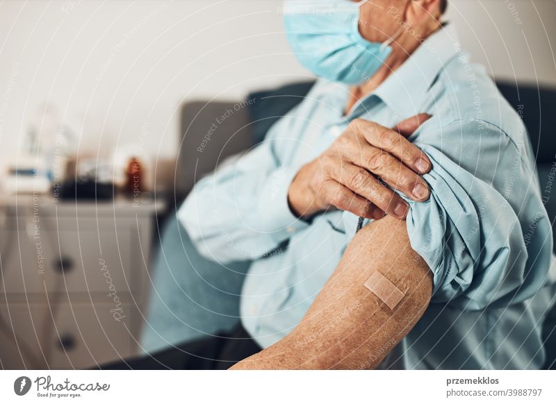 Senior man patient holding shirt sleeve up with a plaster in place of injection of vaccine. Covid-19 or coronavirus vaccination person hospital senior medical