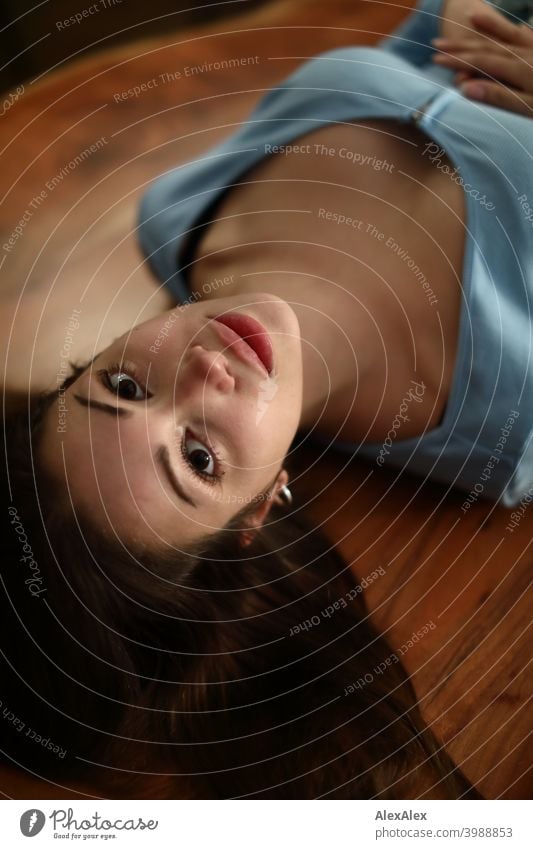 Overhead portrait of a young brunette woman with a light blue top lying on a wooden table and looking up at the camera Young woman pretty Brunette Long-haired