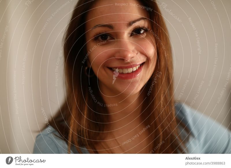 Portrait of a young, brunette, broadly smiling woman with a light blue top in a bright room Young woman pretty Smiling Joy Brunette Long-haired daintily