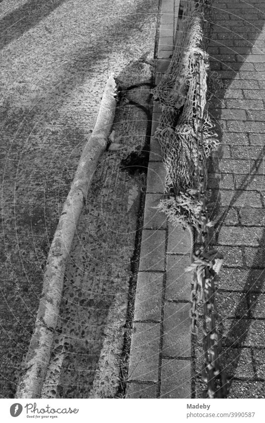 Fishing nets hanging over an old rusty iron chain at the harbour of Neuharlingersiel at the coast of the North Sea near Esens in the district of Wittmund in East Frisia in Lower Saxony, photographed in classic black and white