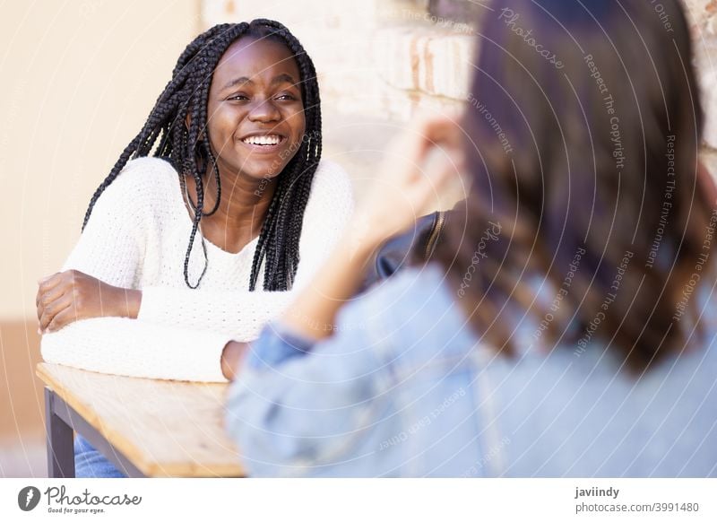 Two multiethnic friends talking sitting at a table outside a bar. woman outdoors multiracial happiness girl friendship happy smile young beautiful lifestyle