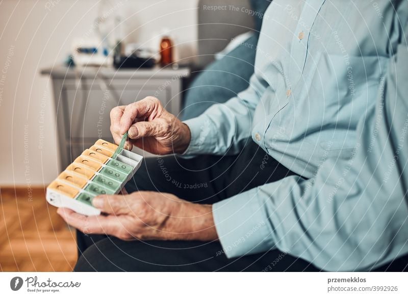 Senior man patient opening pill dispenser to take next medicine dose. Organising medication person hospital senior medical illness nurse sick care clinic