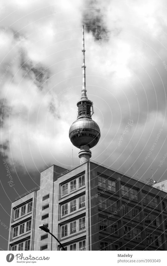 The Berlin TV tower behind a cubic office building with clouds in sunshine at Alexanderplatz in the capital Berlin, photographed in classic black and white