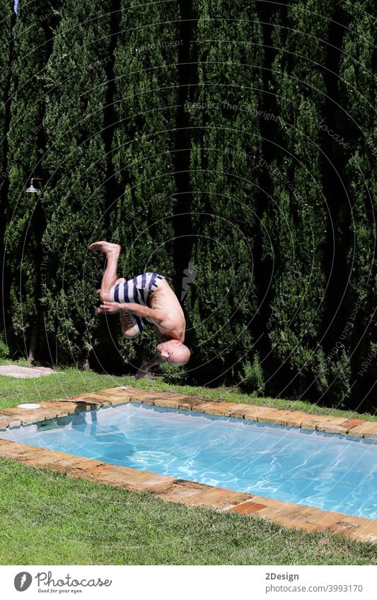 A man is jumping into the pool somersault. Upside down, jump into the water. falling swimming male vacation sunglasses shirtless bald swimsuit poolside leisure