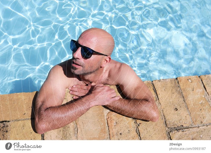 handsome guy half-naked cheerful man smiling laughing in blue water swimming pool wet tanned bald sunglasses summer young happy outside relaxation relaxing