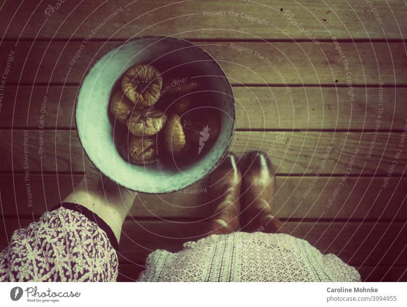 Woman in dress and boots stands on a wooden floor and holds a bowl of dried figs in her hand Figs shell Fruit Fresh Food Healthy Mature cute Organic Juicy