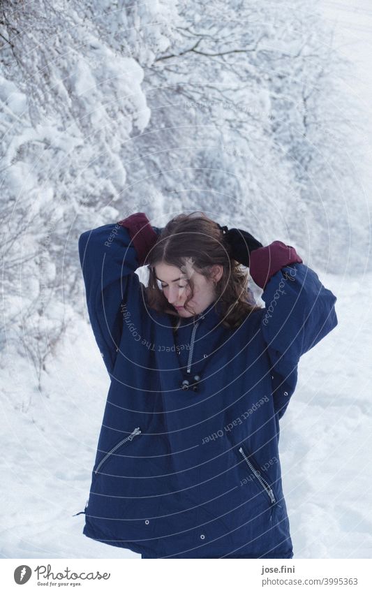 Young woman with warm clothes, looking down, hands above her head, snow in the background. one person young adult Girl Youth (Young adults) Feminine portrait