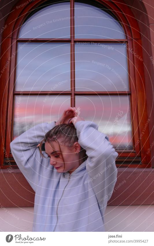 Young woman standing with hands above her head in front of an old building window reflecting the sunset Woman Youth (Young adults) Braids Hair and hairstyles