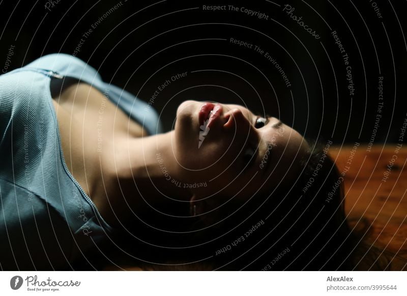 Portrait of a young beautiful brunette woman lying on a wooden table in a dark room looking upwards Young woman pretty Brunette Long-haired Slim teenager