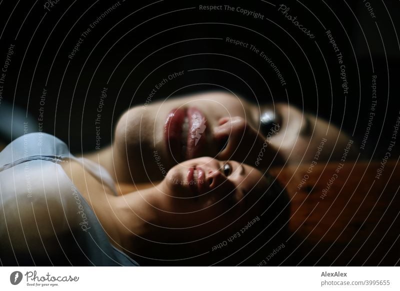 Double exposure - portrait of a young beautiful brunette woman lying on a wooden table in a dark room looking upwards Young woman pretty Brunette Long-haired