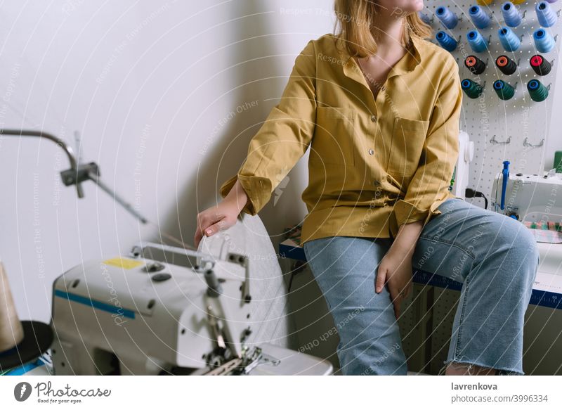 Faceless shot of young female in yellow shirt sitting in her sewing workshop in front of the colorful threads woman seamstress machine textile tailor overlock