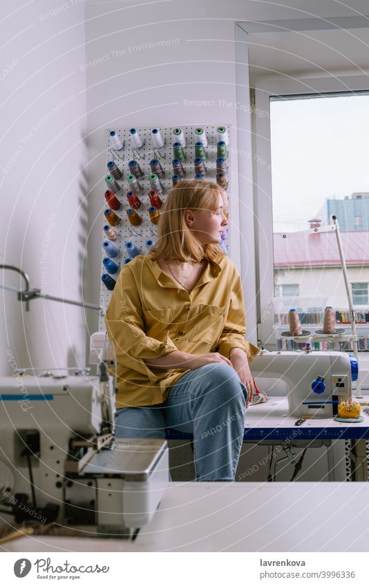 Young female in yellow shirt sitting in her sewing workshop in front of the colorful threads and sewing machines woman seamstress textile tailor overlock