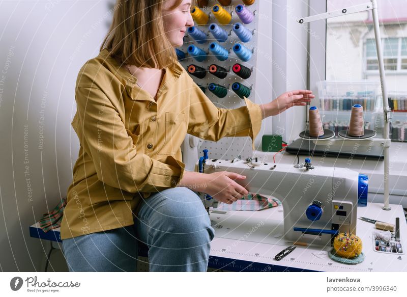 Young woman in yellow shirt sits in her sewing workshop in front of the colorful threads and the sewing machine Woman Sewer Machinery textile Tailor Overlock