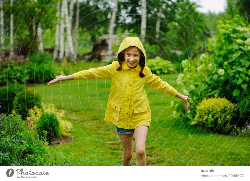 happy kid girl in yellow raincoat playing and having fun in summer garden under the rain child outdoor weather boot rainy waterproof wet little nature childhood