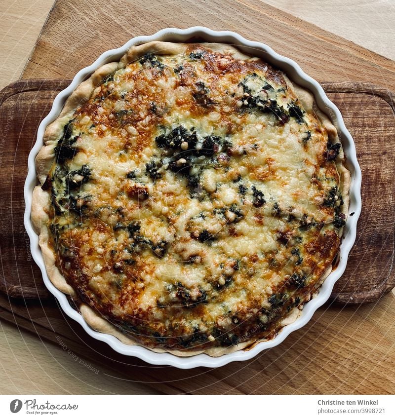 Homemade delicious tart with kale and raw smoked ham, topped with cheese. The tart pan is on wooden board. Bird's eye view. Kale Kale Tart raw ham spicy