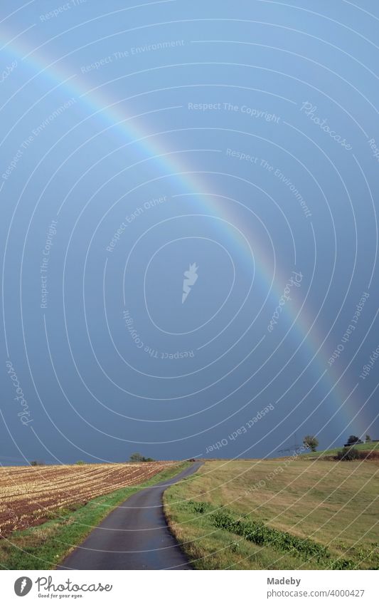 Road between meadows and fields with a rainbow in front of a dark sky on the horizon in autumn in Gembeck at Twistetal in the district of Waldeck-Frankenberg in northern Hesse