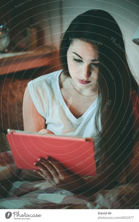 Teen sits in bed with his computer and looks intently at the display Ipad teenager Girl Computer use Homework School coronavirus Quarantine pandemic at home