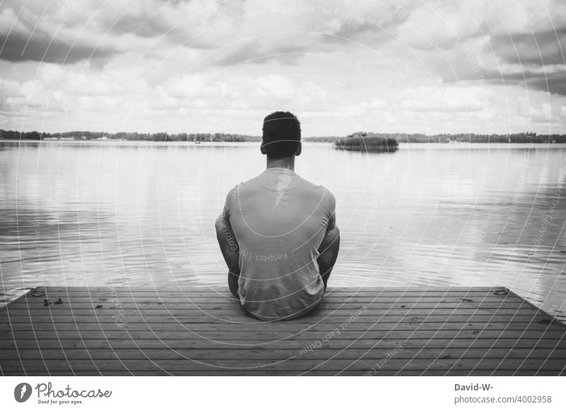 Man sits lonely and alone on a jetty at the lake and enjoys the silence tranquillity Relaxation silent Footbridge Lake gap Meditative Sit To enjoy Loneliness