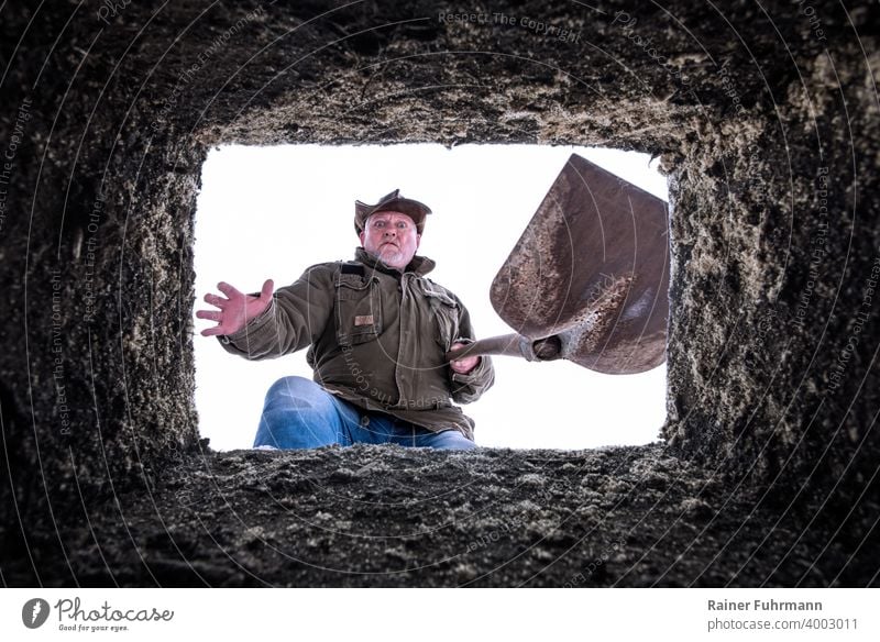 A man with a shovel stands at an open grave. He looks into the depths in horror. Grave Funeral Bury Epidemic pandemic covid-19 Virus Risk of infection