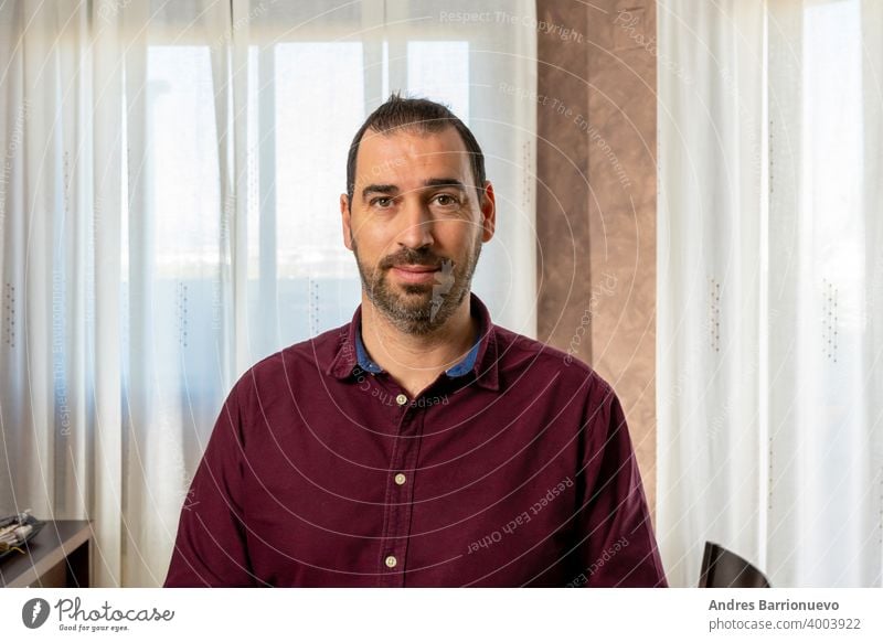 Hispanic handsome man in a purple shirt posing and gesturing fun in the living room at home with white curtains background look indoors bright mouth casual