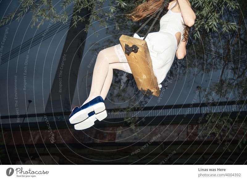 A woman dressed in white outfit with her extremely long legs swinging under the bridge. The sky is dark blue, and the mood is fine. Her fashionable blue shoes are shining from far away.